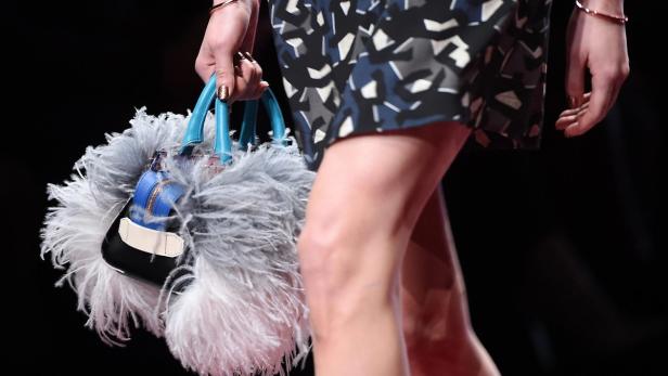 Eine Frau trägt eine Handtasche mit Federn und blauen Henkeln.