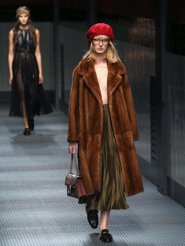 Eine Frau mit roter Baskenmütze und braunem Pelzmantel auf einem Laufsteg.