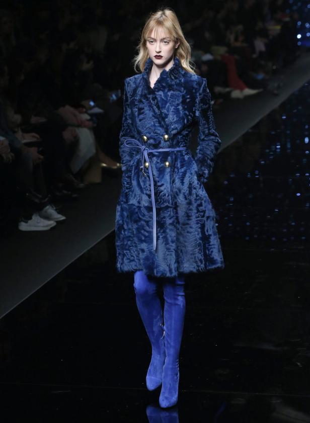 Eine Frau in einem blauen Mantel und passenden Stiefeln auf einem Laufsteg.