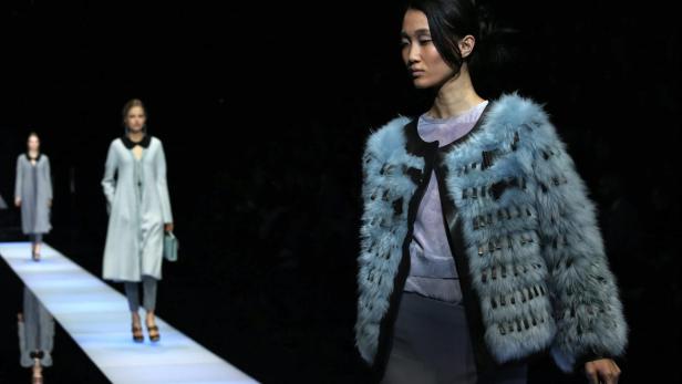 Eine Frau präsentiert auf einem Laufsteg eine hellblaue Jacke mit Fellbesatz.