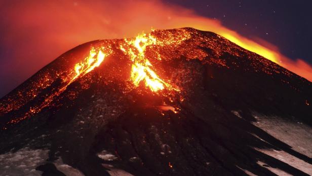 Ein Vulkan bricht aus und Lava fließt den Hang hinunter.
