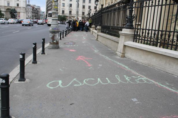 Auf einem Bürgersteig in der Stadt sind mit Kreide Nachrichten und Pfeile gemalt.