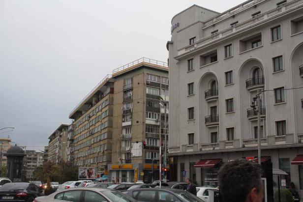 Straßenszene mit Wohnhäusern und geparkten Autos an einem bewölkten Tag.