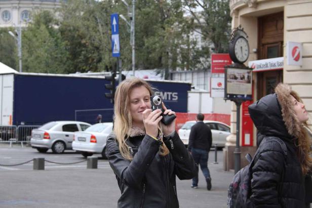 Eine Frau filmt mit einer kleinen Videokamera auf einer belebten Straße.