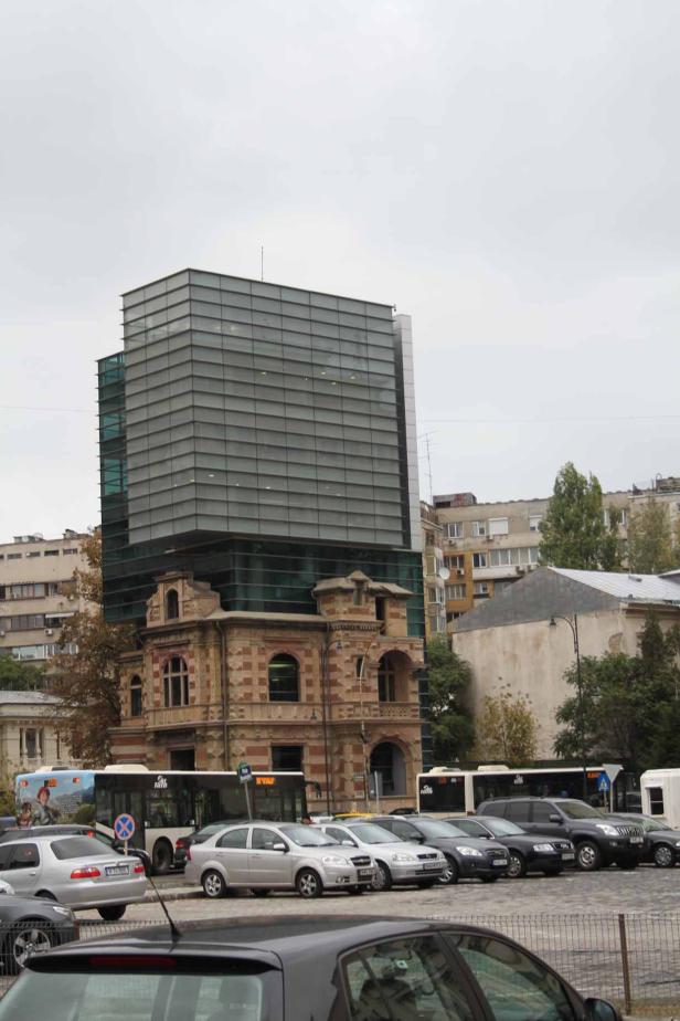 Ein modernes Bürogebäude erhebt sich über einem historischen Gebäude in einer Stadt.