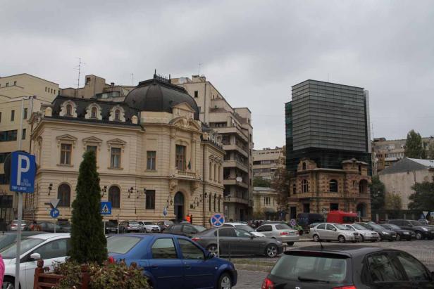 Ein belebter Stadtplatz mit historischen Gebäuden und modernen Bauten unter bewölktem Himmel.