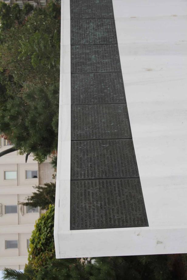 Ein Denkmal mit Inschriften steht vor Bäumen und einem Gebäude.