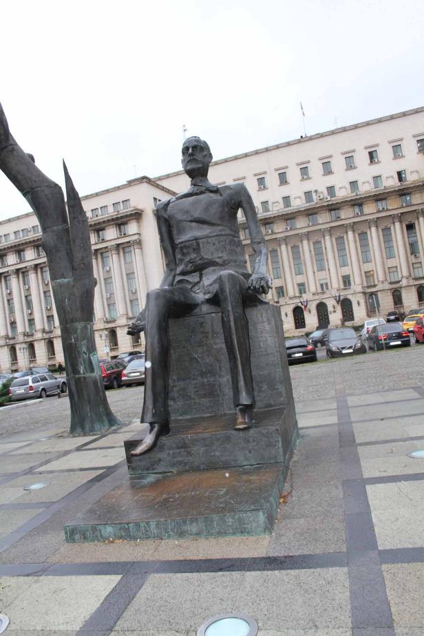 Eine Bronzestatue eines sitzenden Mannes vor einem Gebäude.