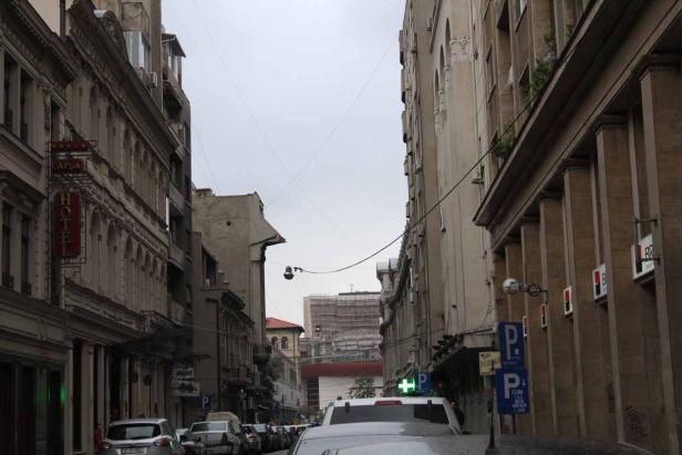 Blick auf eine Straße mit geparkten Autos und alten Gebäuden an einem trüben Tag.