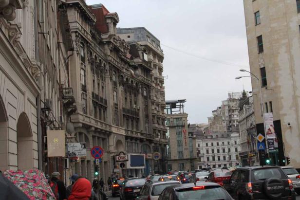 Eine belebte Straße in Bukarest mit alten Gebäuden und viel Verkehr.
