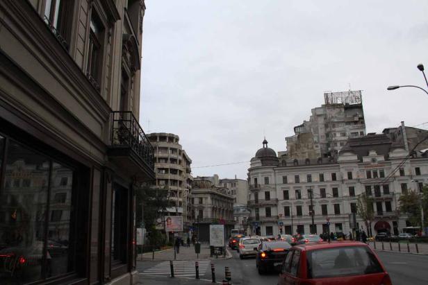 Straßenszene in Bukarest mit verschiedenen Gebäuden und regem Verkehr.