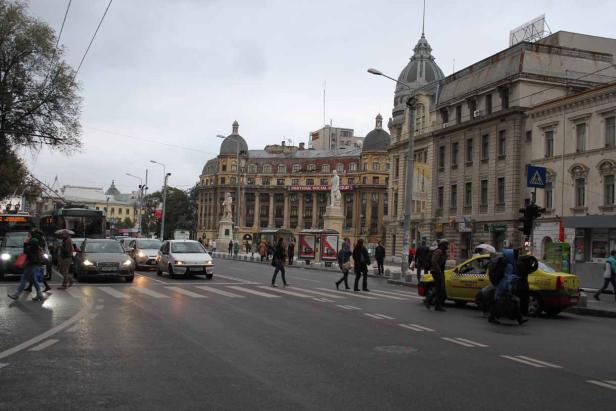 Eine belebte Straße in Bukarest mit Fußgängern, Autos und historischen Gebäuden.