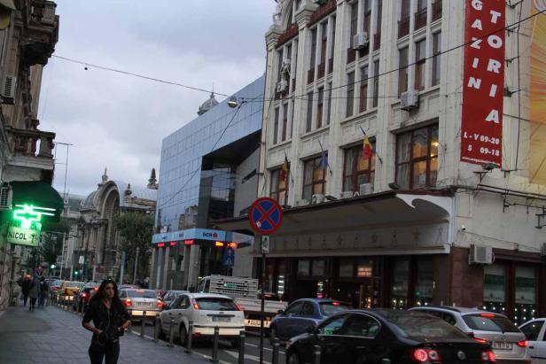 Eine belebte Straße in Bukarest mit Autos und Passanten.