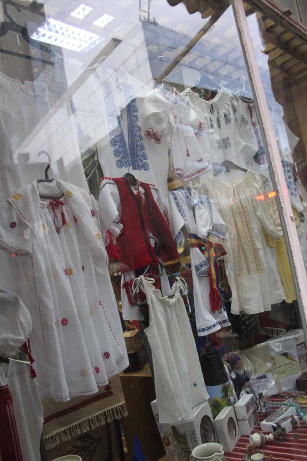 Ein Schaufenster zeigt traditionelle rumänische Kleidung, darunter bestickte Blusen und Westen.