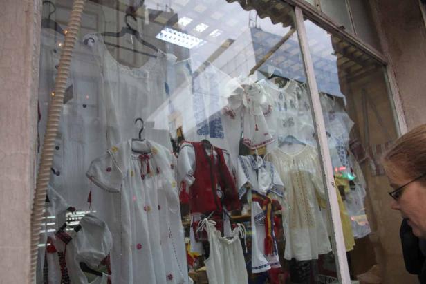 Ein Schaufenster mit traditioneller rumänischer Kleidung wird von einer Frau betrachtet.