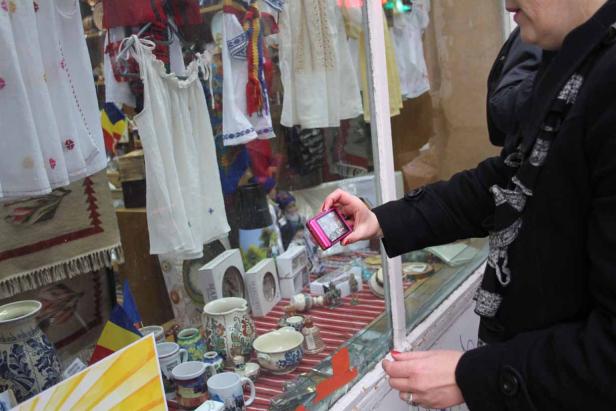 Eine Frau fotografiert mit einer pinkfarbenen Kamera ein Schaufenster mit rumänischer Handwerkskunst.
