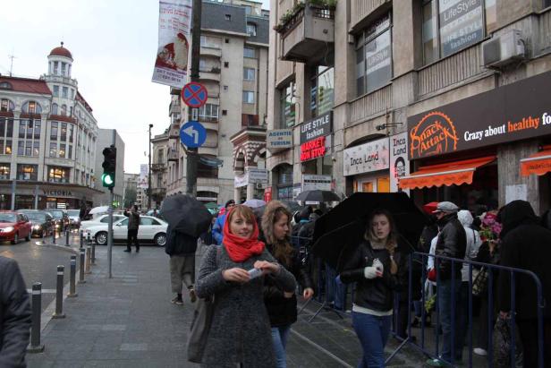 Menschen mit Regenschirmen gehen an einem regnerischen Tag in Bukarest die Straße entlang.