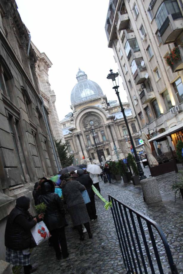 Menschen mit Regenschirmen gehen auf einer Straße in Bukarest entlang eines historischen Gebäudes.