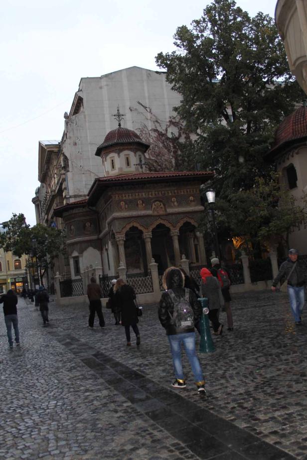 Menschen gehen an einer verzierten Kirche auf einem Kopfsteinpflasterplatz vorbei.