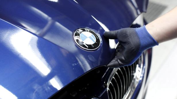 Eine Hand mit Handschuh berührt die Motorhaube eines blauen BMW.
