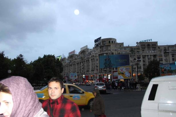 Blick auf die belebte Piața Unirii in Bukarest mit Passanten und einem gelben Taxi.