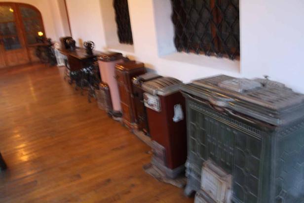 Eine Reihe von alten Öfen und Nähmaschinen in einem Raum mit Holzboden.