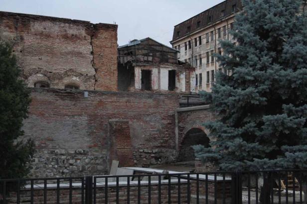 Eine teilweise zerstörte Backsteinmauer und ein Gebäude mit einem blauen Baum im Vordergrund.