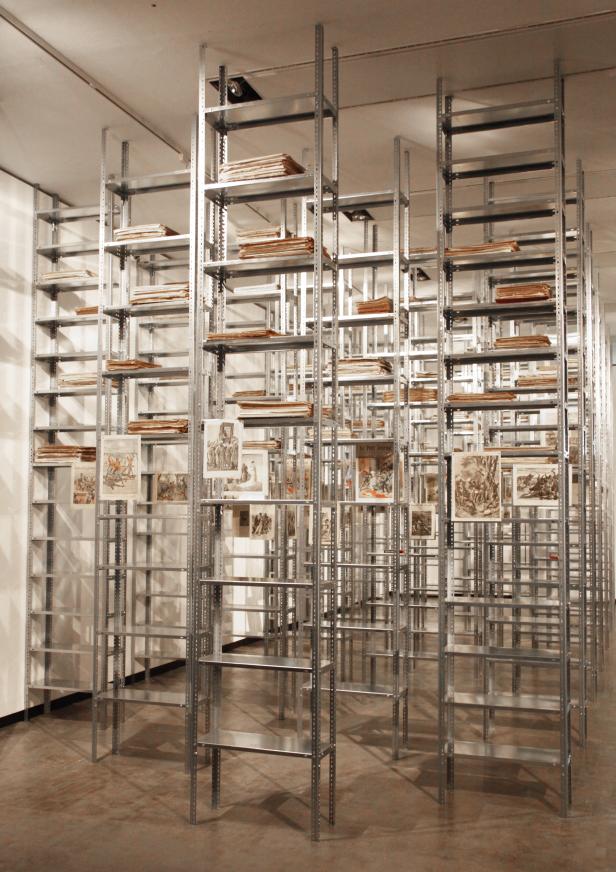 Ein Raum voller hoher, metallener Regale mit Büchern und Bildern.