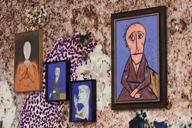 An einer Wand hängen vier gerahmte Gemälde mit abstrakten Darstellungen von Figuren.
