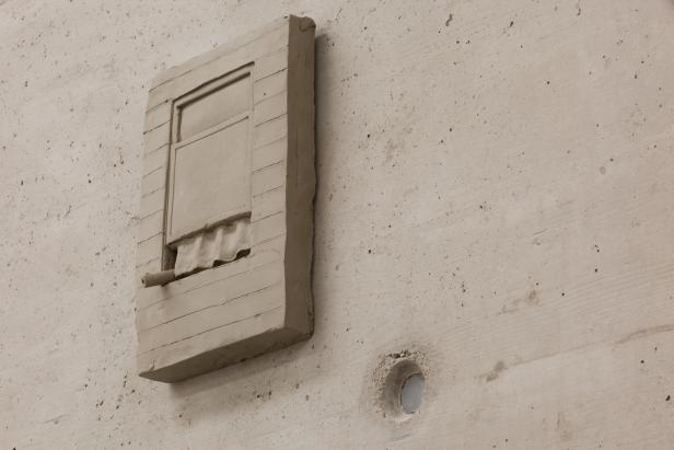 Eine Skulptur aus hellem Ton an einer Betonwand.