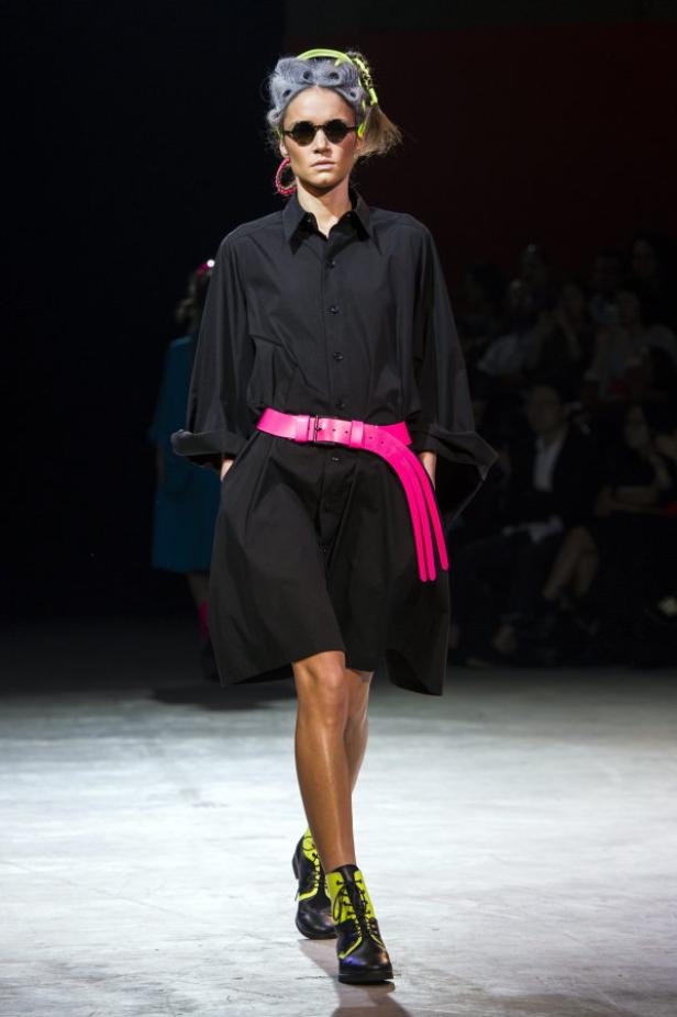 Eine Frau mit Sonnenbrille und neonfarbenem Gürtel läuft auf dem Laufsteg.