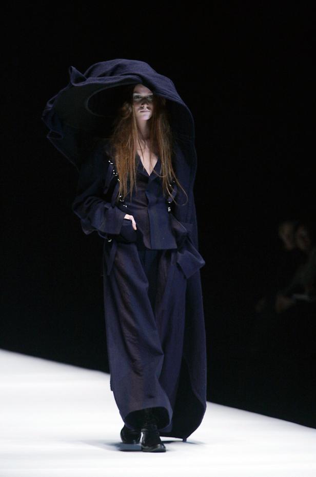 Eine Frau mit einem übergroßen Hut und dunkler Kleidung auf einem Laufsteg.