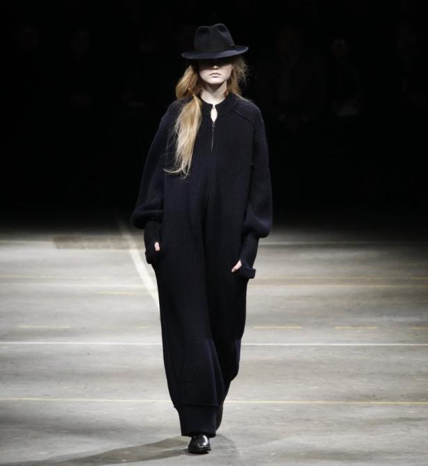 Eine Frau mit Hut und langem, dunklem Strickkleid auf einem Laufsteg.