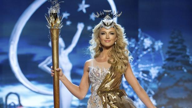 Eine Frau mit Krone und goldenem Kleid hält einen verzierten Stab in der Hand.