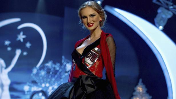 Eine Frau mit blonden Haaren und rotem Kleid lächelt vor einem blauen Hintergrund.