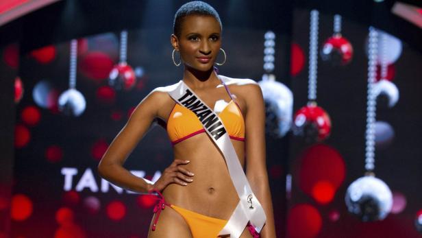 Eine Frau mit einer Schärpe mit der Aufschrift „Tanzania“ posiert in einem orangefarbenen Bikini.