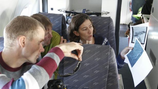 Drei Personen sitzen in einem Flugzeug und betrachten Fotos von Wasserlandschaften.