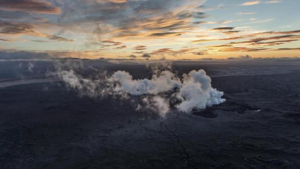 Dampf steigt aus einer vulkanischen Landschaft unter einem bewölkten Himmel bei Sonnenuntergang auf.