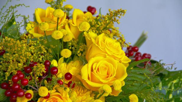 Ein Arrangement aus gelben Rosen, Craspedia und roten Beeren.