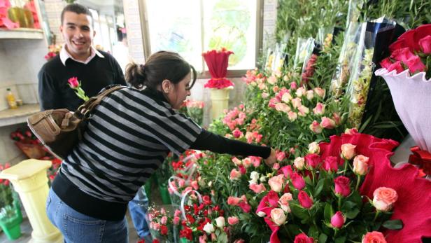 In einem Blumenladen wählt eine Frau Rosen aus, während ein Mann ihr eine einzelne Rose reicht.