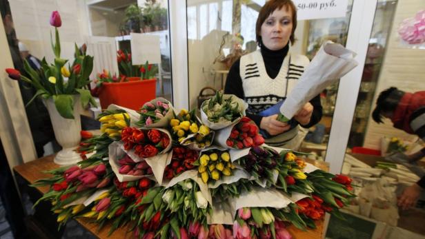 Eine Floristin steht vor einem Tisch voller bunter Tulpensträuße.