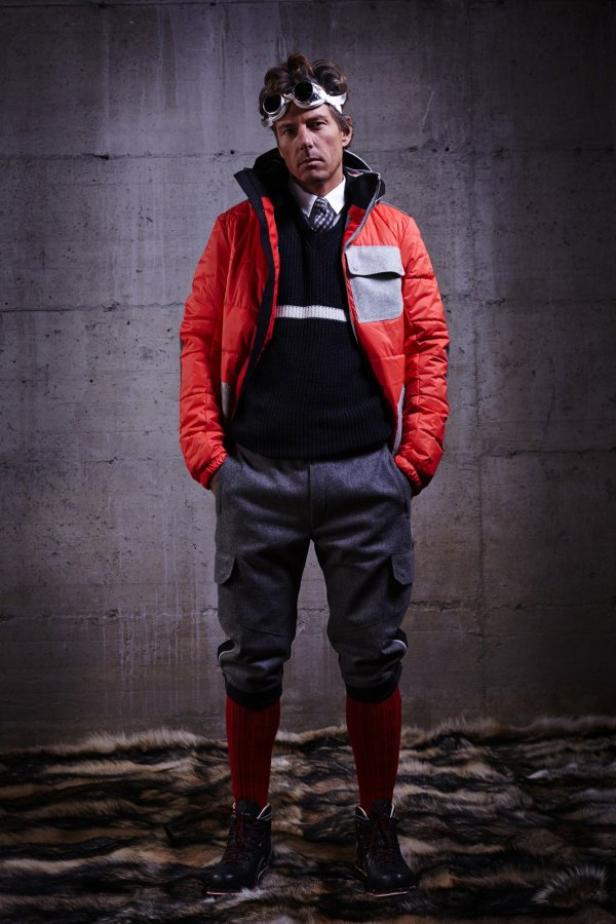Ein Mann mit Skibrille und roter Jacke posiert vor einer Betonwand.