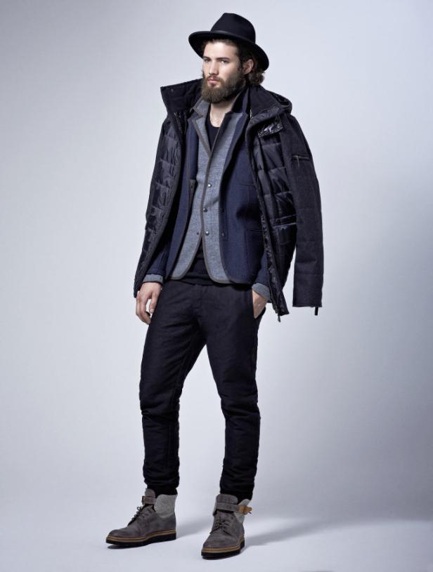 Ein bärtiger Mann mit Hut trägt eine Jacke, ein Sakko und Stiefel.