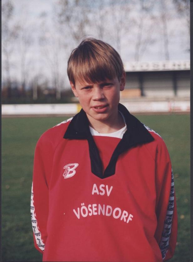 Ein junger Mann im roten Trikot des ASV Vösendorf steht auf einem Sportplatz.