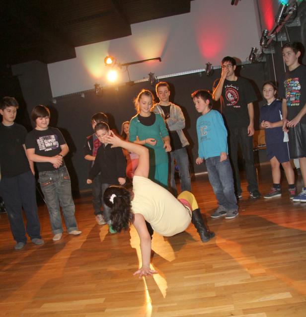 Ein junges Mädchen macht einen Handstand vor einer Gruppe von Jugendlichen auf einer Bühne.