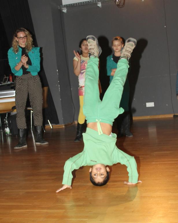 Ein Junge macht einen Handstand auf einem Holzboden, während andere zusehen.