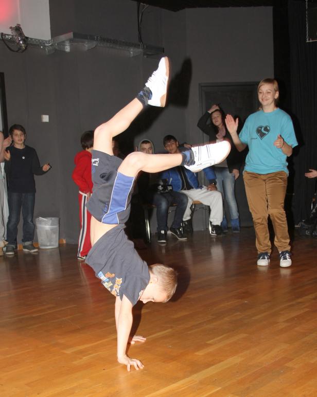 Ein Junge macht einen Handstand auf einer Bühne, während andere zusehen.