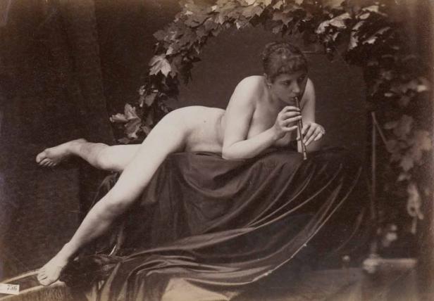 Eine nackte Frau liegt auf einem Tuch und spielt Flöte.