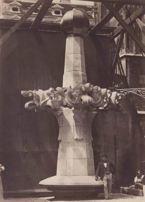 Ein großes, verziertes Steinelement, möglicherweise ein Kirchturmspitz, mit zwei Männern im Hintergrund.