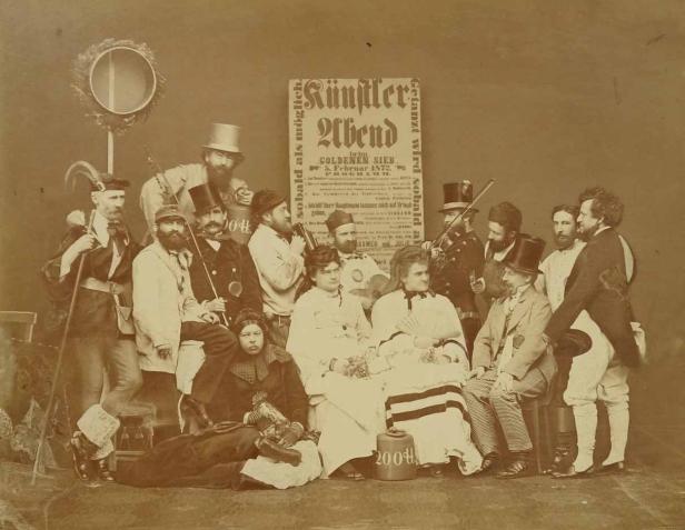 Eine Gruppe von Männern und Frauen posiert für ein Foto vor einem Plakat für einen Künstlerabend.